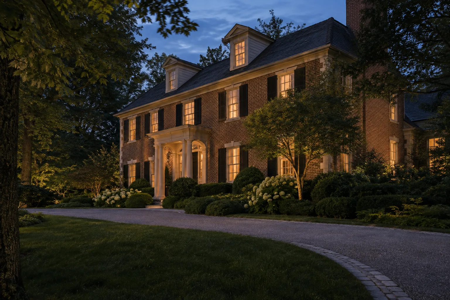 Brick residence with selectively illuminated facade and mature trees at blue hour