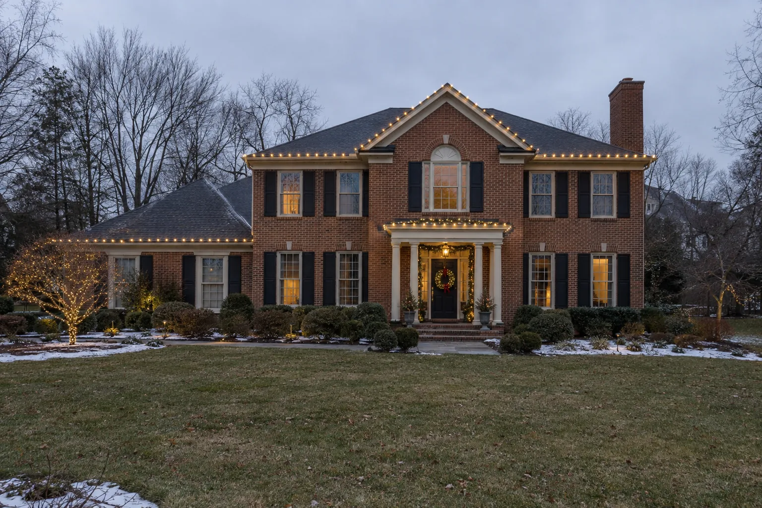 traditional brick home with coordinated roofline lighting, a lit garden tree and entrance greenery