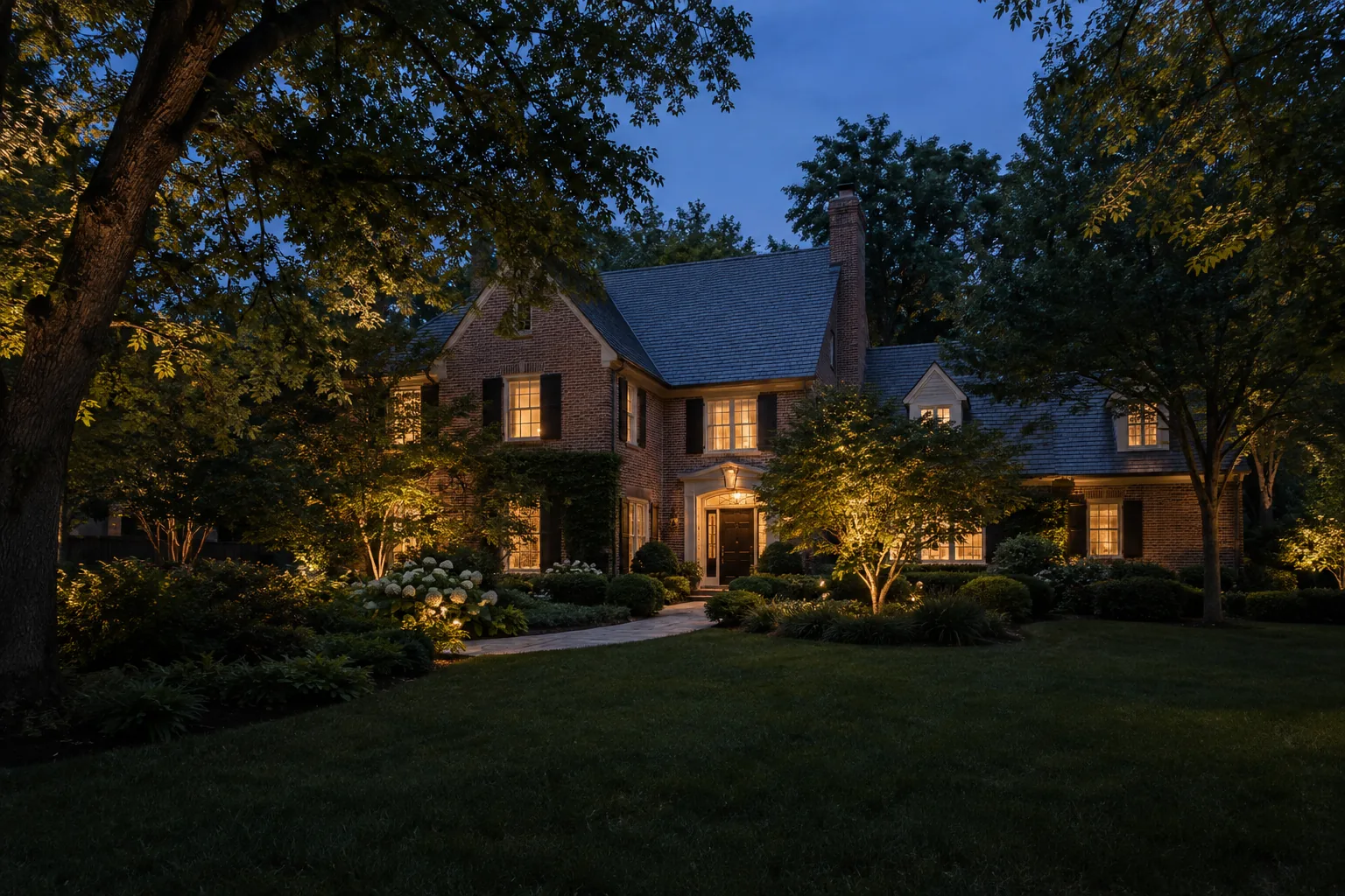 Brick home framed by softly illuminated trees and a warm, welcoming front path at blue hour